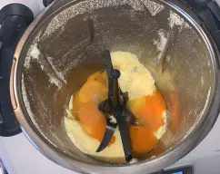 Step <p>Pon en el vaso del Thermomix el azúcar y la piel de naranja y programa 10 segundos a velocidad 10. Baja los restos de las paredes. Coloca la mariposa en las cuchillas y añade el huevo y las yemas y bate 4 minutos a velocidad 3,5.</p> illustration